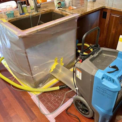 Professional drying equipment with tunnel containment in place to dry a kitchen island after a sink malfunction, minimizing demolition